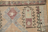 Distressed pile of an Oushak rug with geometric patterns in dusty rose and cantaloupe.