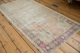 Distressed Oushak rug runner corner with low pile, vibrant pink floral border, and pale field.