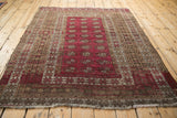 Anatolian vintage rug corner, showing raspberry Bokhara-style gul motifs, brown, ivory geometric borders, fringe.