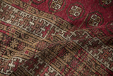 Textured fold of a hand-knotted Anatolian rug, displaying geometric motifs in deep raspberry, brown, and ivory.