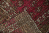 Folded corner of vintage Anatolian rug, revealing deep raspberry red gul motif pile and brown foundation.