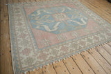 Distressed vintage Oushak rug showing muted blue medallion and pink geometric border motifs.