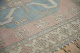 Distressed Oushak border shows geometric patterns, pastel tones, and braided pale green fringe.