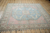 Distressed Oushak rug corner showing geometric border, pink field, braided red and green fringe.