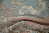 Distressed Oushak rug's worn pile texture featuring geometric blue, pink, and beige motifs.
