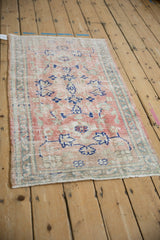Angled view of distressed Oushak rug, showing worn rose field and faded blue floral vinery.