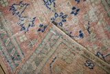 Detailed fold of a distressed Oushak rug, showing worn pile with rose, ivory, and blue patterns.