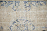 Distressed vintage Oushak rug showing cream foundation and faded blue floral motif wear.