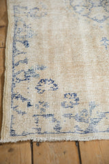 Vintage Distressed Oushak rug corner showing worn cream pile, visible foundation, blue design.
