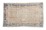 Vintage distressed Oushak rug with a dusty cobalt blue roundel medallion and border on a faded cream field.