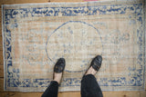 A person's view of a distressed vintage Oushak rug, showing its low pile and faded pattern for scale.