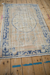 Angled view of a vintage Oushak rug highlighting its worn texture and faded blue medallion.