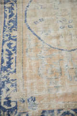 Close-up on the distressed Oushak pile, showing wear to the knot heads and blue arabesque border.