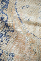 A folded view highlights the distressed texture and low hand-knotted pile of a vintage Oushak rug.