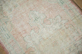 Distressed Oushak rug pile detail, featuring pale pink, ivory, jade green hues, and a secured edge.