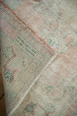 Folded corner of vintage distressed Oushak rug, showing pale pink and green pile, exposed foundation.
