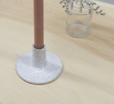 A dusty pink taper candle in a wide, white speckled ceramic holder.