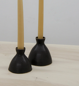 Two handmade matte black ceramic taper holders with light beige candles.