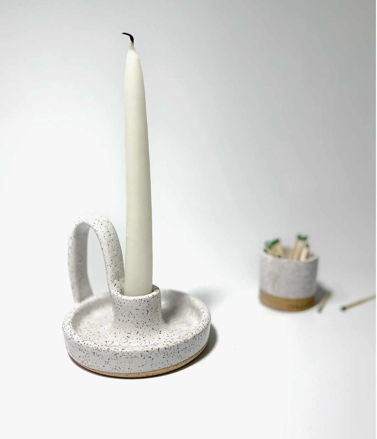 White speckled ceramic taper holder with loop, natural clay base, holding a white candle.