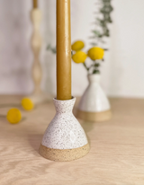 Handmade white speckled ceramic taper candle holder with natural unglazed clay base, holding a golden candle.
