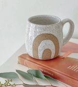 Medium handmade ceramic mug with speckled white glaze and tan wax resist rainbow design.