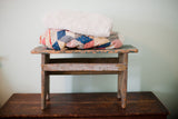 A primitive wooden stool bench with a distressed, chippy turquoise and white painted finish.
