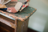 Detailed view of the primitive stool's weathered corner with a chippy turquoise painted finish.