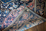Folded antique Farahan Sarouk rug displays hand-knotted weave, royal blue, and salmon border.