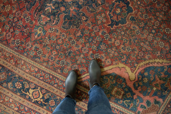 Angled view of an antique Persian rug's oversized arabesque patterns in red and navy blue.