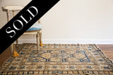 A styled antique Caucasian rug displaying its neutral-toned geometric pattern and blue accents.