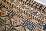 Small holes and wear visible within the geometric border of an antique Caucasian rug.