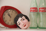 Mid-century ceramic head art piece displayed on a shelf with vintage decor for context.