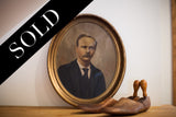 The vintage painted portrait in its distressed gold oval frame, displayed on a wooden shelf.