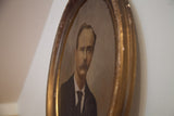 Angled view of the vintage portrait of a father in its aged, curved oval frame.