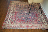 Angled view of an antique Kerman rug with a mellow red and blue prayer design.