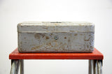 Front of a rusty gray metal tool box with its central keyhole lock and industrial patina.