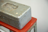 Angled view of the gray metal tool box lid, showing the handle and weathered industrial patina.