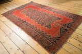 4x6 antique tomato red Malayer rug with a navy blue central medallion, shown from an angle.