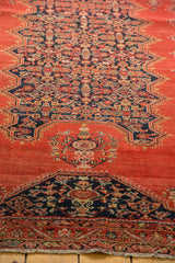 Angled view of antique Malayer rug with intricate dark blue Herati motif on a tomato red field.