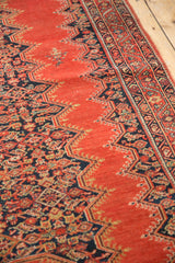 Angled view of an antique Malayer rug's tomato red field and dark blue Herati pattern.