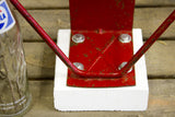 Detail of chippy red industrial metal hoop bolted to white wooden base.