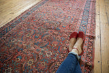 Angled view of an antique Persian Bakshaish rug showing its faded allover Herati pattern in russet and blue.