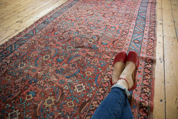 Angled view of an antique Persian Bakshaish rug showing its faded allover Herati pattern in russet and blue.