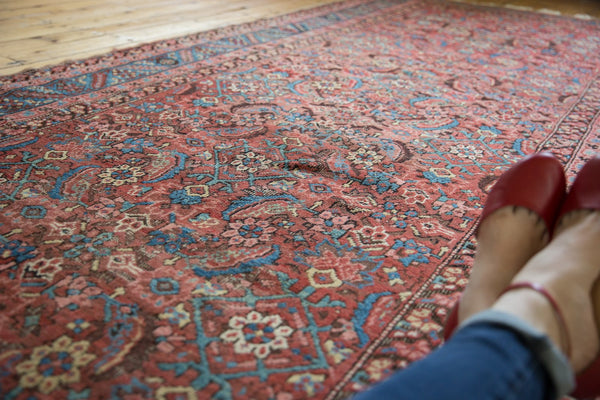 Angled close-up of the worn wool pile and herati pattern in faded red and blue on the antique Bakshaish rug.