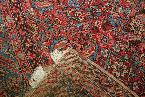 Antique Persian Bakshaish rug with corner folded back to show the woven foundation and white fringe.