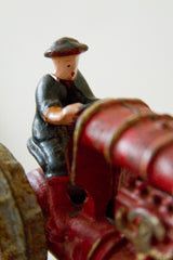 Vintage cast iron driver figure in black hat on a worn red tractor.