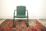 Vintage dark green metal outdoor kids tulip chair with industrial style and visible rust.