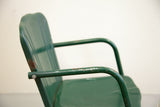Angled close-up of mid-century green metal chair back, showing ribbed texture and rust.