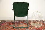 Dark green metal kids tulip chair back, showing weathered paint and surface rust.