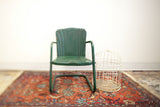 Green metal kids tulip chair with aged patina, beside a white birdcage and antique rug.